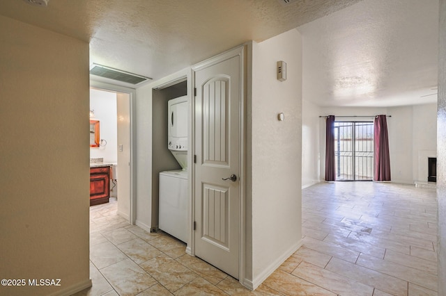 hall with stacked washer / dryer, visible vents, a textured ceiling, and baseboards