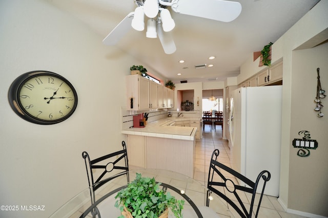 kitchen featuring tile countertops, light tile patterned floors, decorative backsplash, freestanding refrigerator, and a peninsula