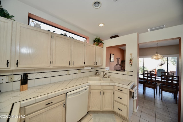 kitchen with tile countertops, white dishwasher, a sink, hanging light fixtures, and decorative backsplash