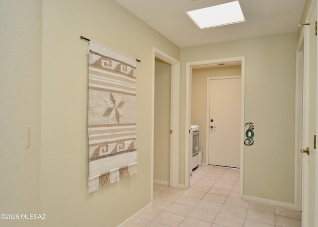 corridor featuring light tile patterned floors, washer / clothes dryer, a skylight, and baseboards