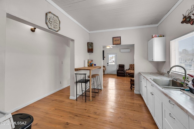 kitchen featuring an AC wall unit, sink, white cabinets, ornamental molding, and light hardwood / wood-style floors