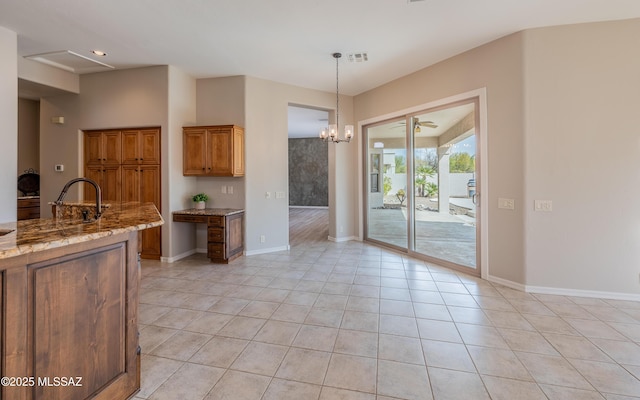 kitchen with hanging light fixtures, light stone countertops, ceiling fan with notable chandelier, light tile patterned floors, and sink