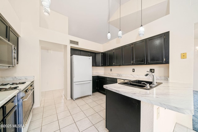 kitchen featuring pendant lighting, sink, light stone countertops, gas range oven, and white fridge