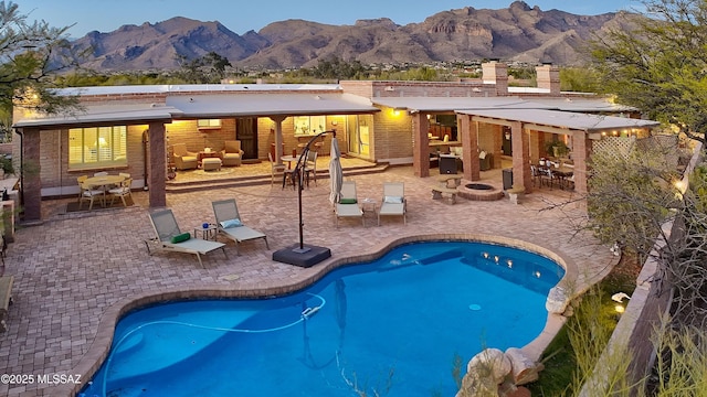 view of swimming pool with a patio, a mountain view, and an outdoor living space with a fire pit