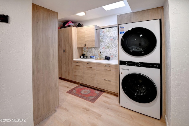 clothes washing area featuring cabinets, stacked washer and clothes dryer, a skylight, and light wood-type flooring