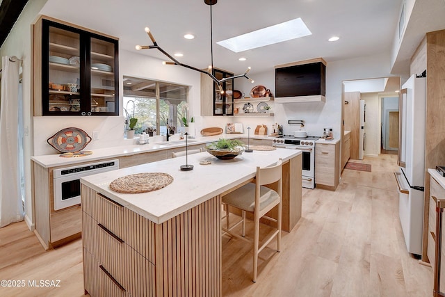 kitchen with light hardwood / wood-style floors, a center island with sink, white appliances, and a skylight