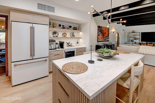 kitchen with a kitchen island, beverage cooler, light stone counters, paneled refrigerator, and light hardwood / wood-style flooring