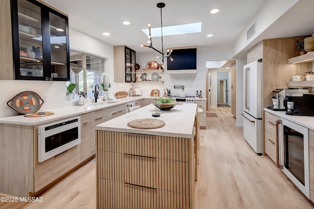 kitchen with a kitchen island, sink, hanging light fixtures, stainless steel appliances, and light wood-type flooring