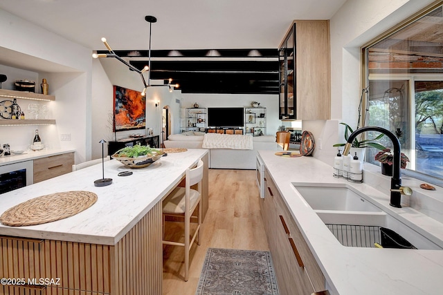 kitchen with decorative light fixtures, sink, beverage cooler, a center island, and light hardwood / wood-style flooring