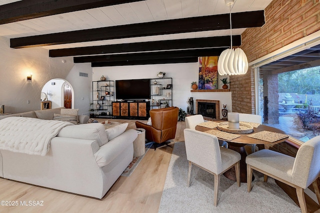 living room with beam ceiling, brick wall, a fireplace, and light hardwood / wood-style floors