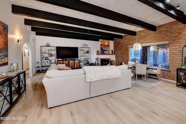 living room featuring brick wall, a fireplace, beam ceiling, and light wood-type flooring