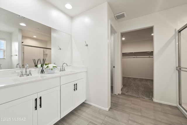 full bathroom with double vanity, visible vents, a walk in closet, and a sink