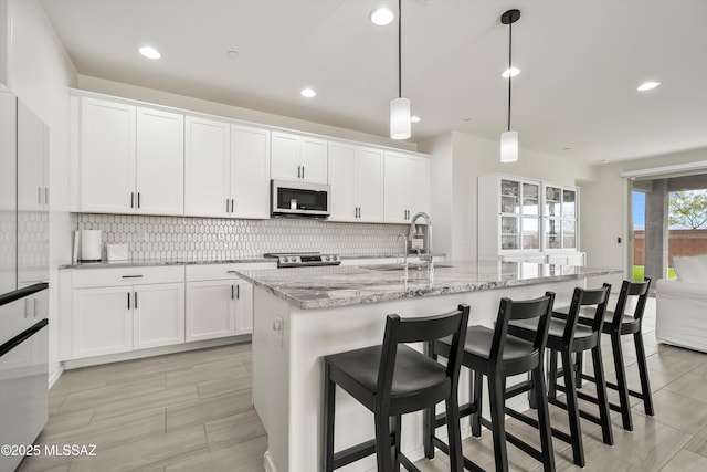 kitchen featuring decorative light fixtures, a sink, a center island with sink, and white cabinetry