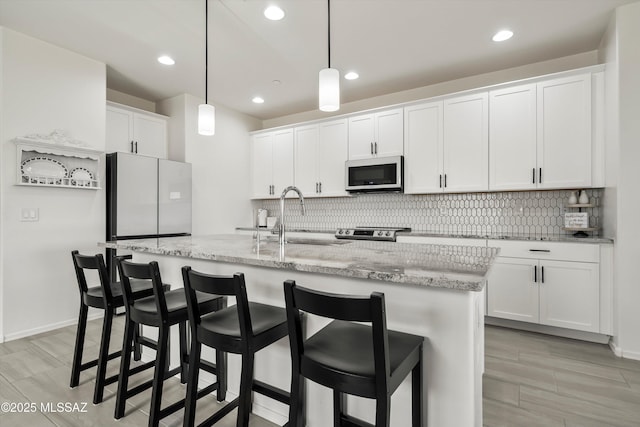 kitchen with a center island with sink, white microwave, hanging light fixtures, white cabinetry, and a sink
