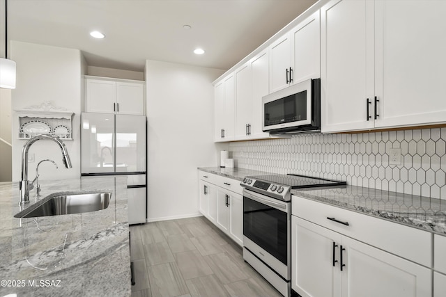 kitchen with light stone counters, a sink, white cabinetry, electric stove, and decorative backsplash