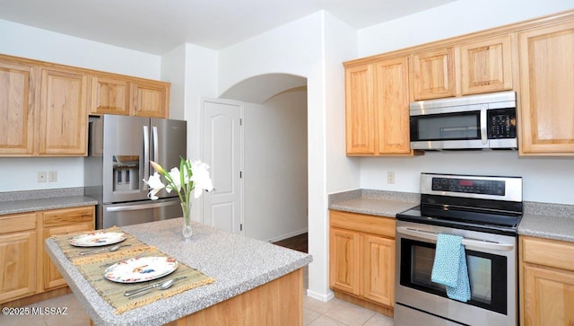 kitchen featuring a center island, appliances with stainless steel finishes, light stone countertops, and light brown cabinetry