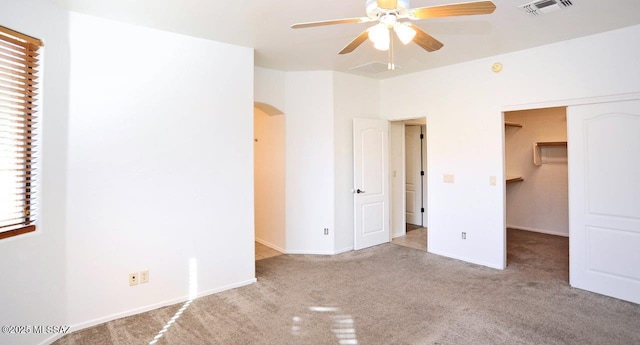 unfurnished bedroom featuring ceiling fan, a closet, a walk in closet, and light colored carpet