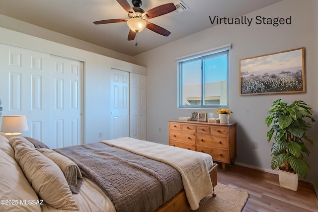 bedroom featuring wood finished floors, baseboards, visible vents, ceiling fan, and two closets