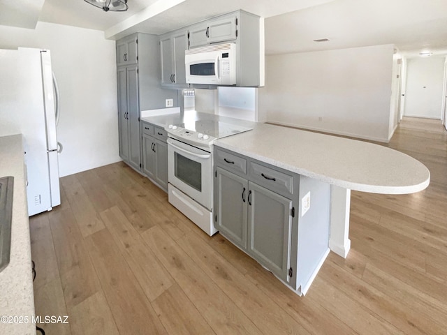 kitchen featuring gray cabinets, a breakfast bar area, white appliances, and kitchen peninsula