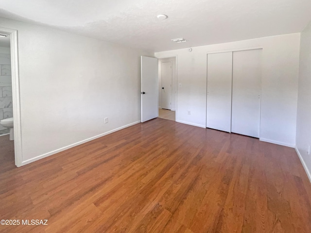 unfurnished bedroom featuring dark wood-type flooring, a closet, and ensuite bathroom