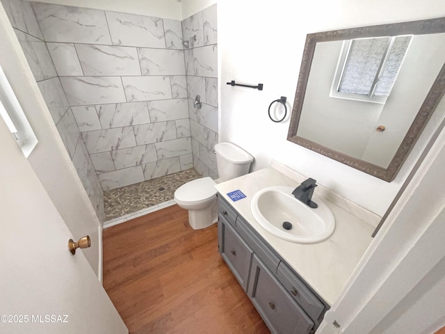 bathroom with a tile shower, vanity, hardwood / wood-style flooring, and toilet