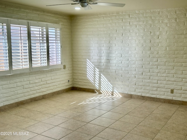 spare room with light tile patterned floors, ceiling fan, and brick wall