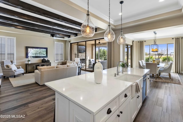 kitchen with hanging light fixtures, an island with sink, light stone counters, white cabinets, and sink