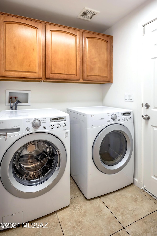 laundry area with cabinets, light tile patterned floors, and washing machine and clothes dryer