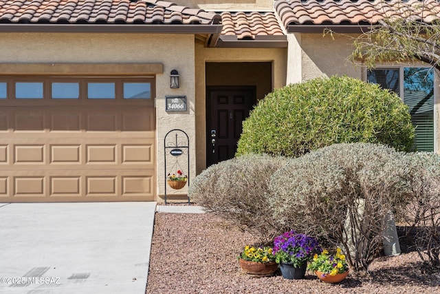 doorway to property with stucco siding, a tiled roof, driveway, and a garage