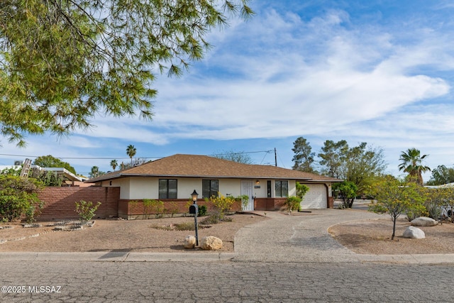 ranch-style house with driveway, fence, a garage, brick siding, and stucco siding