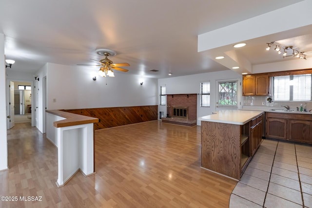 kitchen featuring wood walls, a fireplace, a ceiling fan, open floor plan, and wainscoting