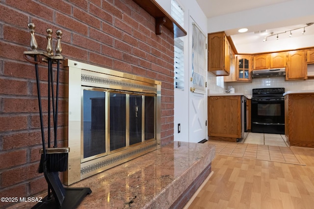 kitchen with under cabinet range hood, black electric range oven, light wood-style flooring, and brown cabinetry
