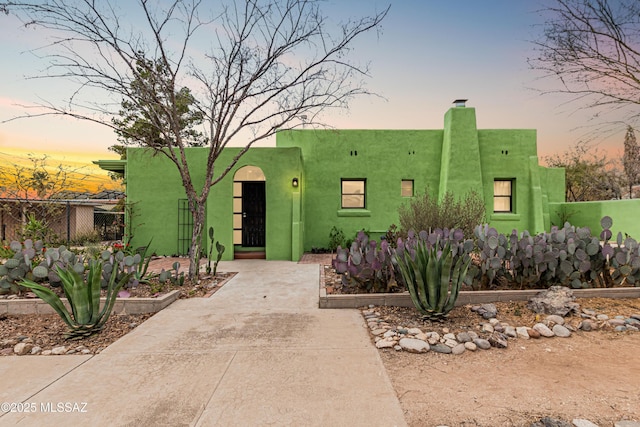 pueblo revival-style home with a chimney, fence, and stucco siding