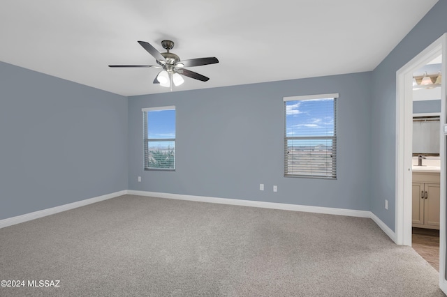 unfurnished bedroom featuring multiple windows, light colored carpet, ceiling fan, and ensuite bathroom