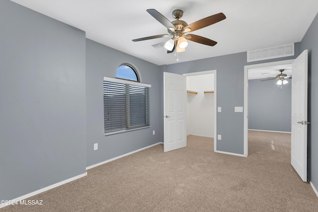 unfurnished bedroom featuring a walk in closet, light colored carpet, and ceiling fan