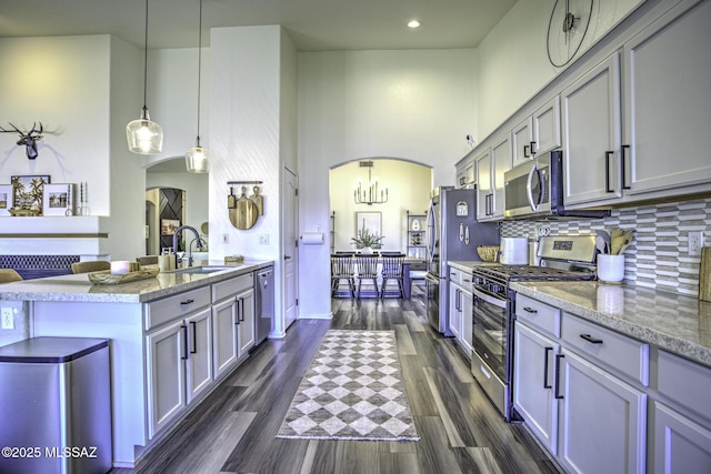 kitchen featuring a sink, appliances with stainless steel finishes, arched walkways, dark wood finished floors, and a high ceiling