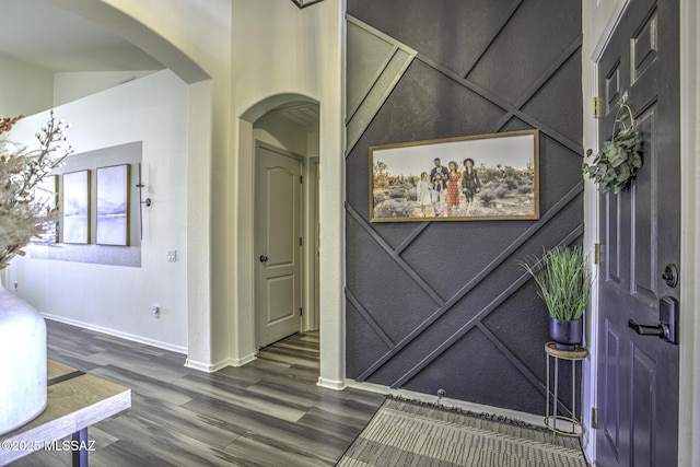 foyer with baseboards, arched walkways, and wood finished floors