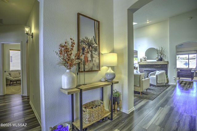 hallway with baseboards, arched walkways, wood finished floors, and a textured wall