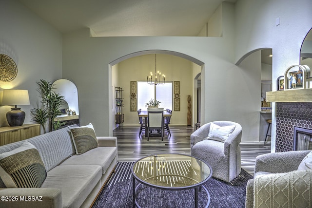 living area with a tiled fireplace, arched walkways, wood finished floors, baseboards, and a notable chandelier