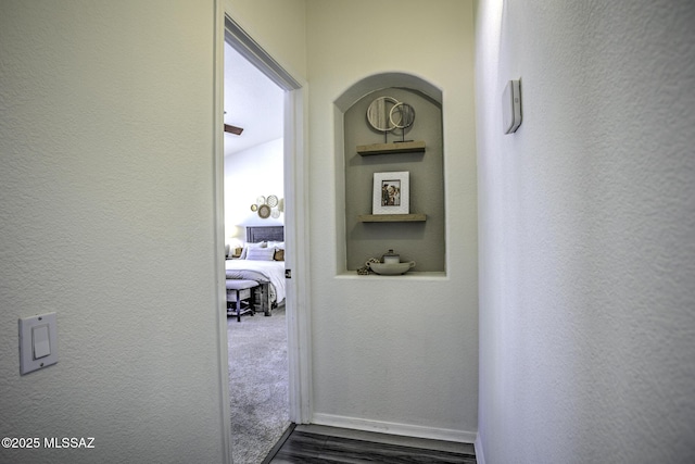 corridor featuring a textured wall, dark wood finished floors, and baseboards