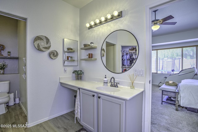 bathroom with baseboards, toilet, wood finished floors, vanity, and a ceiling fan