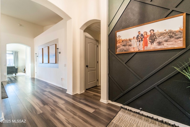 corridor featuring baseboards, arched walkways, and dark wood finished floors