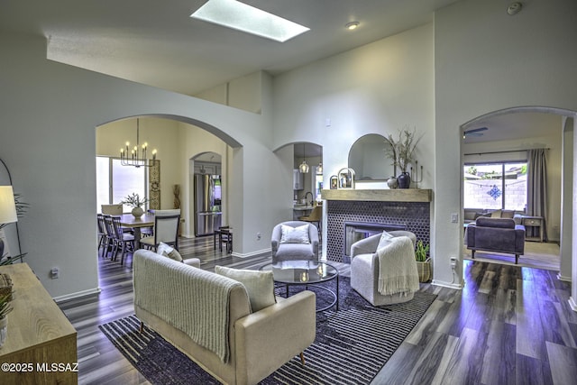 living room featuring wood finished floors, a tiled fireplace, high vaulted ceiling, and baseboards