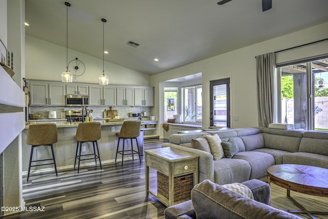 living area with visible vents, lofted ceiling, dark wood-type flooring, and plenty of natural light