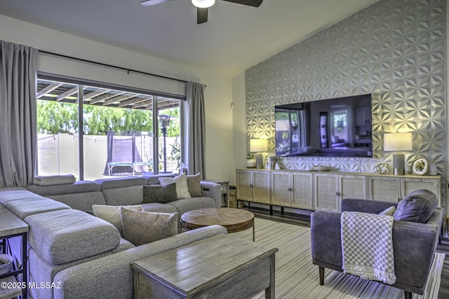 living room featuring an accent wall, wallpapered walls, vaulted ceiling, and ceiling fan