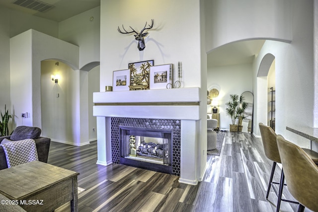 living room with visible vents, baseboards, arched walkways, a fireplace, and wood finished floors