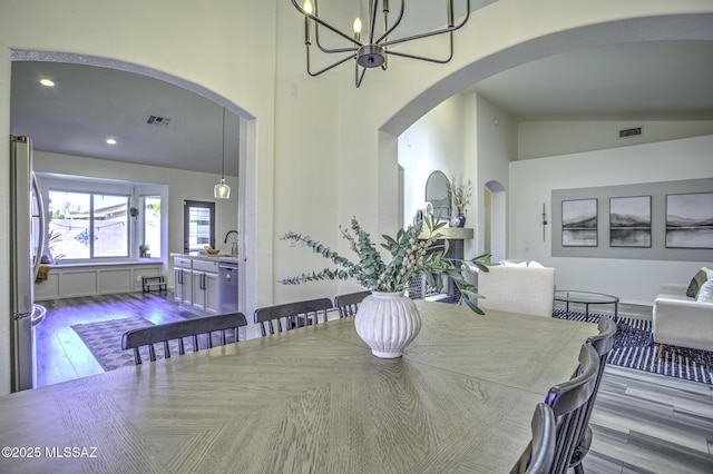 dining space featuring arched walkways, visible vents, wood finished floors, and a chandelier