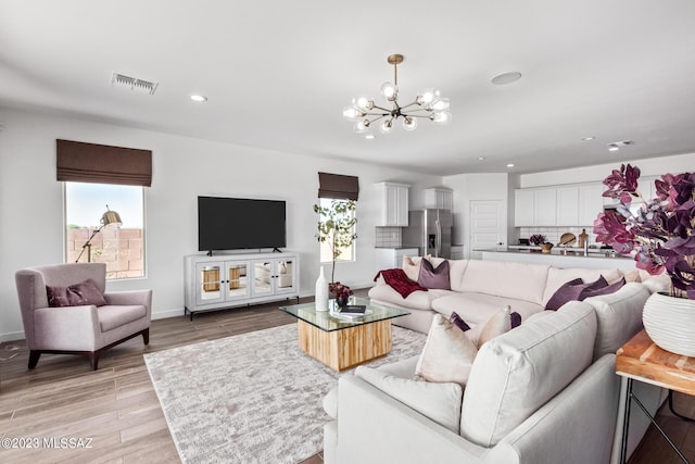 living room with a wealth of natural light, an inviting chandelier, and light hardwood / wood-style flooring