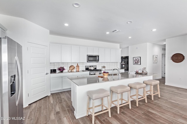 kitchen featuring a kitchen island with sink, visible vents, white cabinets, appliances with stainless steel finishes, and tasteful backsplash