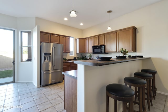 kitchen with light tile patterned flooring, a breakfast bar area, high end refrigerator, hanging light fixtures, and kitchen peninsula